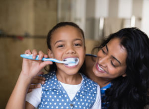 Young girl brushing teeth with mother by her side