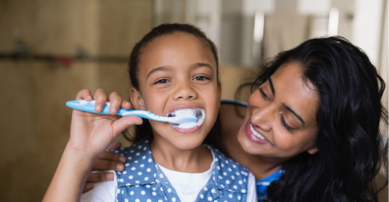 Young girl brushing teeth with mother by her side